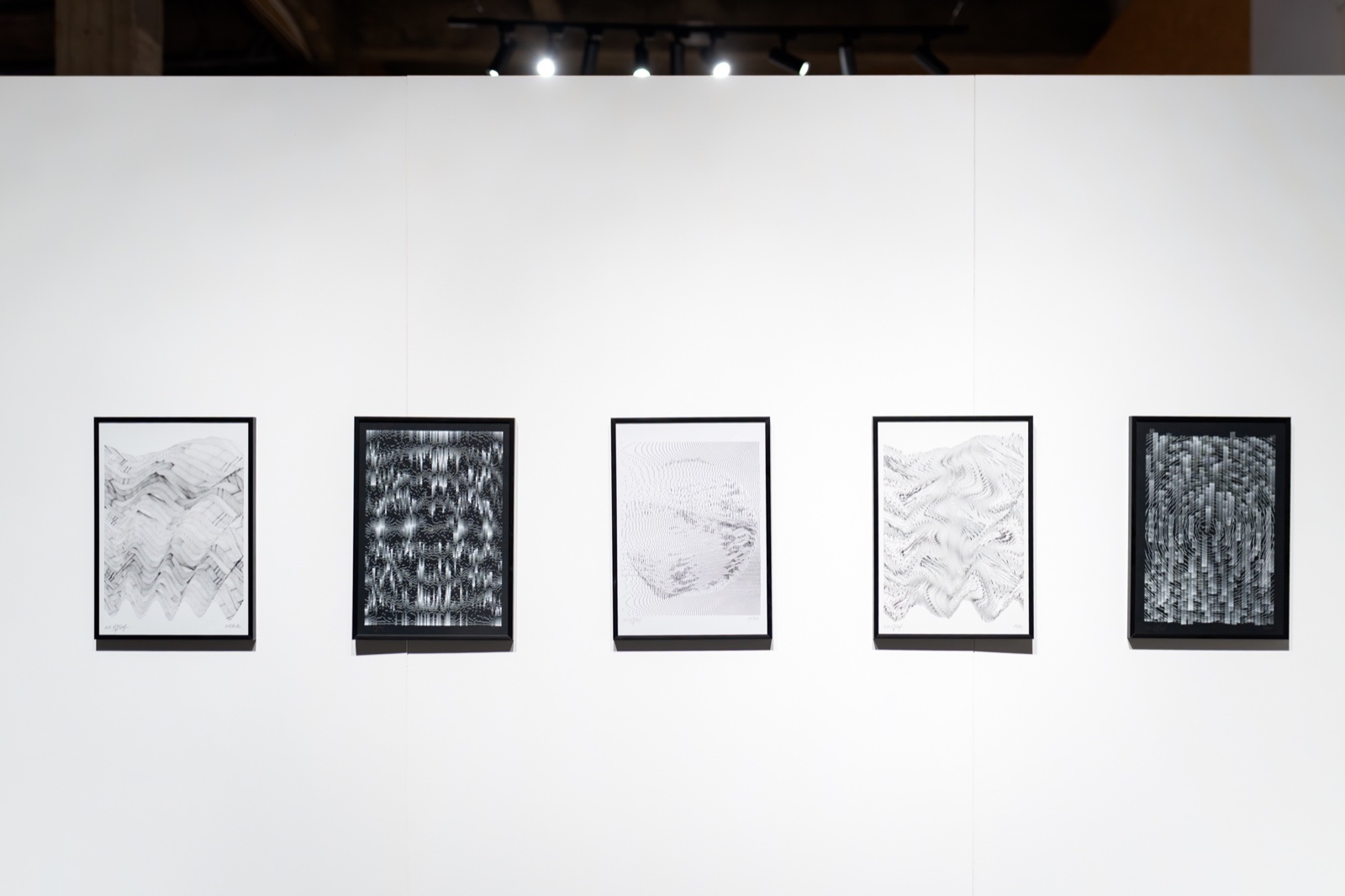 Five framed drawings in a row on a white gallery wall: wave-like patterns of fine black and white lines, two of them on black paper.