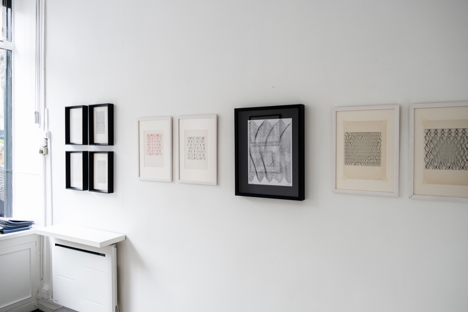 A white gallery wall with framed line drawings: some on aged, yellowed paper, others crisp and new.