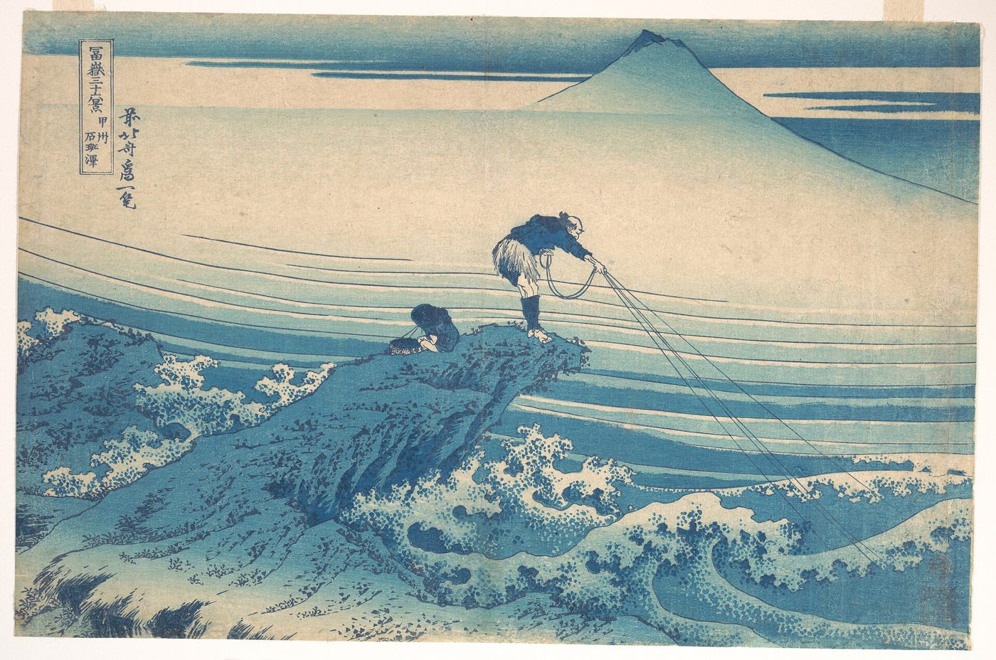 A woodblock print in blue tones of a fisherman on a rock above waves, with Mount Fuji in the background.