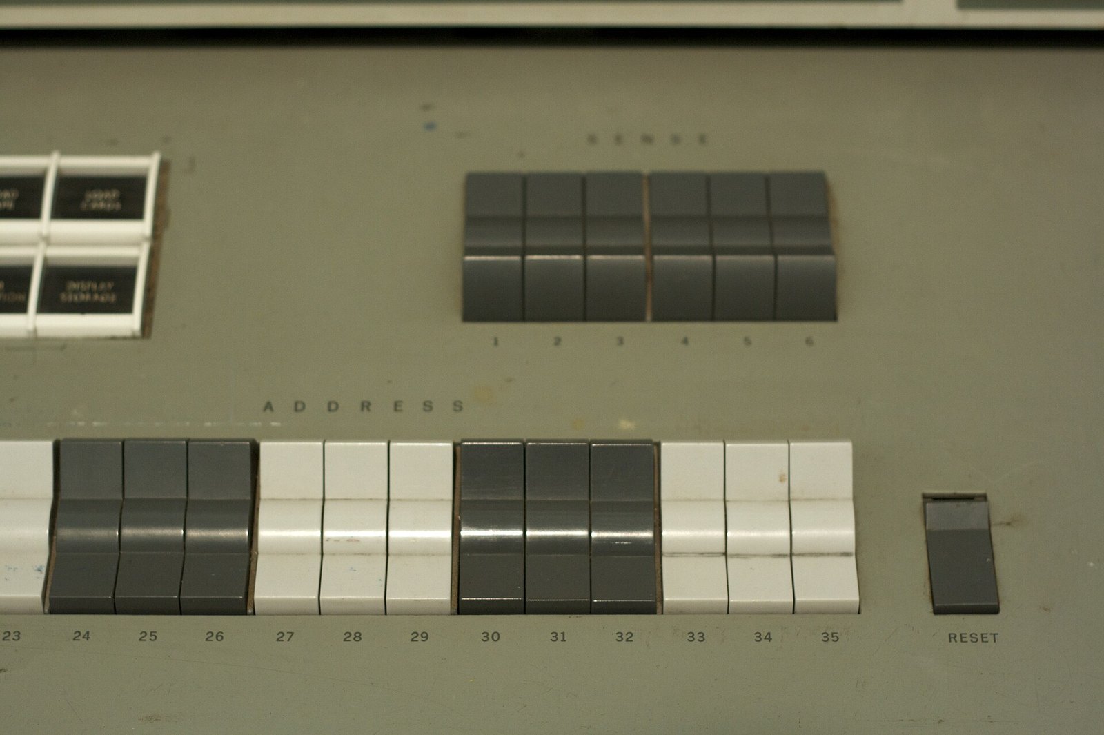 Close-up of a grey computer console with rows of square push buttons in grey and white, labelled Sense, Address and Reset.