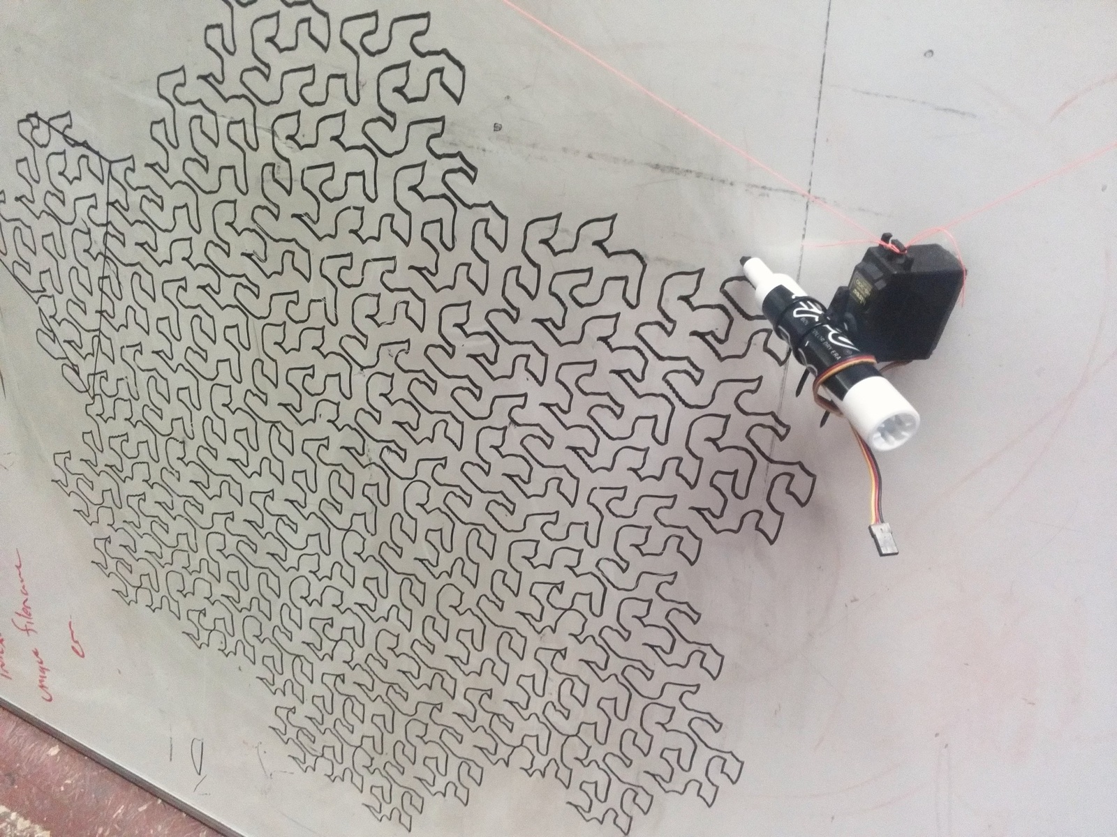 A whiteboard on which a hanging pen has drawn a complex outline like a snowflake, with two strings running up to the corners.
