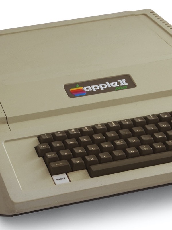 A beige Apple II Plus computer with a built-in dark brown keyboard and a rainbow Apple badge, seen at an angle on a white background.